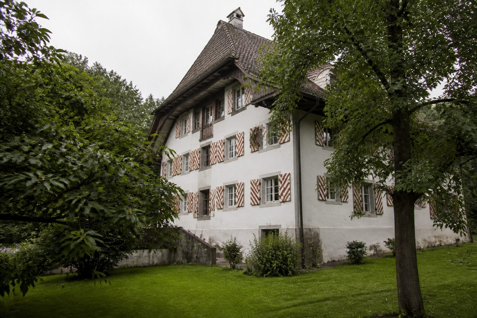 Traditionelles Schweizer Wohnhaus hinter Bäumen – Erbschaft und Immobilienkapital klären